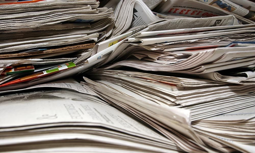 Photo of a stack of newspapers.|Photo of door mat saying